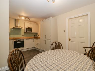 A kitchen with a round table covered with a checkered tablecloth and wooden chairs at Wye Valley Cottage in Symonds Yat