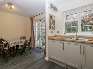 A kitchen with a dining table and chairs next to a glass door and cabinets under a window at Wye Valley Cottage in Symonds Yat