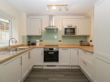 A kitchen with white cabinets wooden countertops a built in oven microwave toaster kettle and a window at Wye Valley Cottage in Symonds Yat