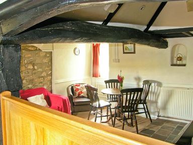 A dining area with a round wooden table surrounded by four chairs and a sitting area with a red armchair and a brown armchair at Gorrig Bwthyn in Llandysul