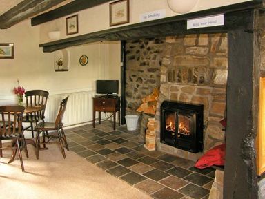 A room with a stone fireplace with firewood and a fire a wooden dining table with chairs and a small television on a stand at Gorrig Bwthyn in Llandysul