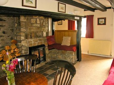 A room with a stone fireplace wood stack a small table with chairs and a built in bench seat at Gorrig Bwthyn in Llandysul