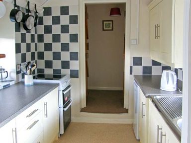 A kitchen with checkered tile walls stove sink kettle and kitchen utensils at Gorrig Bwthyn in Llandysul