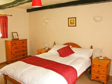 A bedroom with a double bed with red bedding and wooden furniture at Gorrig Bwthyn in Llandysul