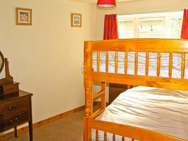 A bedroom with wooden bunk beds a small dresser with a mirror and two pictures on the wall at Gorrig Bwthyn in Llandysul