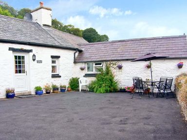 An outdoor patio area with a white door and windows on a white stone building with flower pots and outdoor table with chairs and umbrella at Gorrig Bwthyn in Llandysul