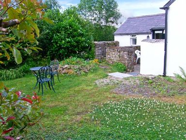A garden with green grass metal table and chairs white house and stone wall at Gorrig Bwthyn in Llandysul