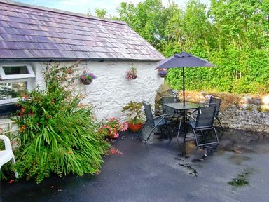 An outdoor patio with a table umbrella chairs and plants beside a white stone wall at Gorrig Bwthyn in Llandysul