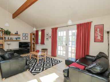 A living room with black leather sofas a wooden coffee table and red curtains at Orchard Lodge in Warkworth