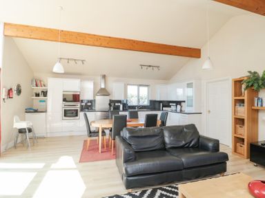 A kitchen and dining area with white cabinets a round wooden dining table with black chairs and a black sofa at Orchard Lodge in Warkworth