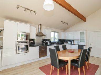A kitchen with white cabinets stainless steel appliances and a wooden dining table with six black chairs at Orchard Lodge in Warkworth