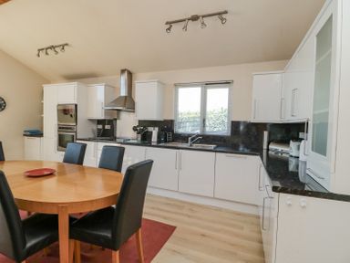 A kitchen with white cabinets black countertops and a wooden dining table with black chairs at Orchard Lodge in Warkworth