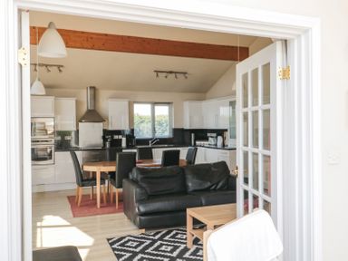 A kitchen and dining area with black chairs around a wooden table a black sofa and a wooden coffee table at Orchard Lodge in Warkworth