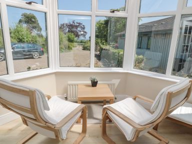 A sunroom with two wooden chairs and a small wooden table with a plant on it at Orchard Lodge in Warkworth