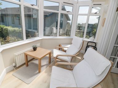 A sunroom with two white cushioned chairs and a wooden table on a rug at Orchard Lodge in Warkworth
