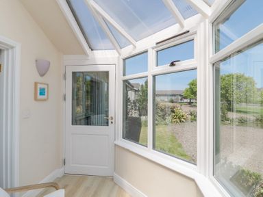A sunroom with windows and a door overlooking a garden at Orchard Lodge in Warkworth