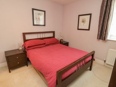 A bedroom with a double bed with red bedding two dark wooden nightstands and framed flower pictures on walls at Orchard Lodge in Warkworth