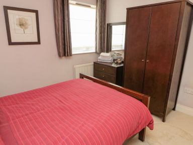 A bedroom with a bed with a red striped duvet a wooden wardrobe and a chest of drawers with folded towels at Orchard Lodge in Warkworth