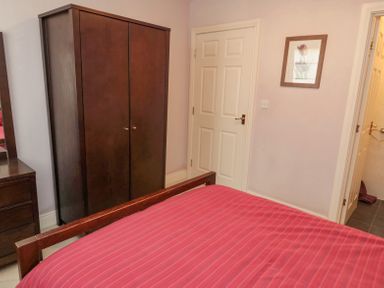 A bedroom with a red bedspread a wooden wardrobe a dresser with a mirror and doors on the walls at Orchard Lodge in Warkworth