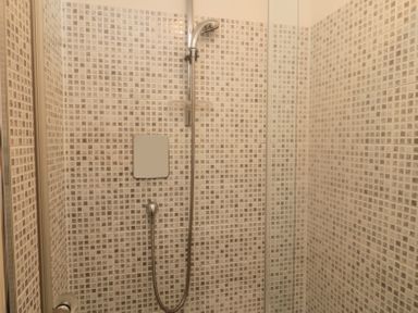 A shower area with wall-mounted shower head and handheld shower on tiled walls at Orchard Lodge in Warkworth