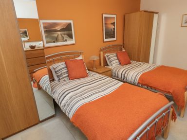A bedroom with two single beds with striped bedding and orange throws at Orchard Lodge in Warkworth