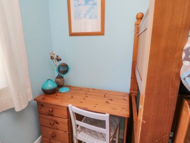 A small wooden desk with drawers a white chair a mirror and decorative items next to a bunk bed in a room at Orchard Lodge in Warkworth