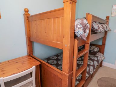 A bedroom with a wooden bunk bed and a wooden desk with a white chair at Orchard Lodge in Warkworth