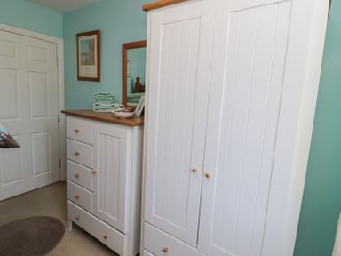 A bedroom corner with white wooden wardrobe and dresser with mirror and folded towels