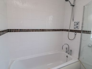 A bathroom with white tiled walls a bathtub a showerhead and a glass shower screen at Orchard Lodge in Warkworth