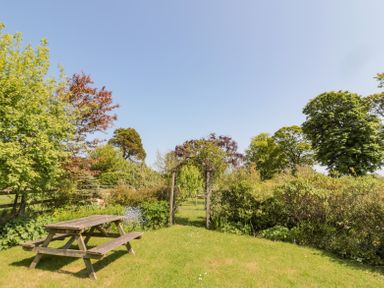A garden area with a wooden picnic table and a wooden arch surrounded by trees and bushes at Orchard Lodge in Warkworth