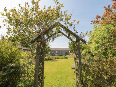 A garden with a wooden arch covered in plants and a lawn leading to a building at Orchard Lodge in Warkworth