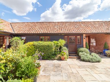 An outdoor patio area with plants and shrubs in front of a building with a tiled roof at Horseshoe in Little Glemham near Wickham Market