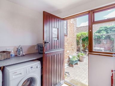 A utility room with a washing machine an iron basket and a wooden door opening to a garden at Horseshoe in Little Glemham near Wickham Market