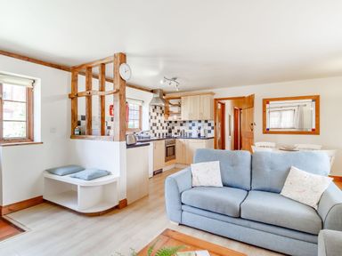 A living room with a blue sofa and kitchen area with wooden cabinets and tiled backsplash at Horseshoe in Little Glemham near Wickham Market