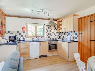 A kitchen with wooden cabinets black and white tiled backsplash and appliances at Horseshoe in Little Glemham near Wickham Market