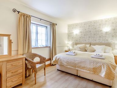 A bedroom with a bed a wicker chair a wooden dresser and curtains at Horseshoe Little Glemham near Wickham Market