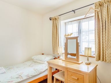 A bedroom with a single bed a wooden dressing table with mirror two lamps and a window with curtains at Horseshoe in Little Glemham near Wickham Market