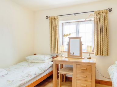 A bedroom with a single bed pillow a wooden dressing table with mirror and lamps under a window with curtains at Horseshoe Little Glemham near Wickham Market