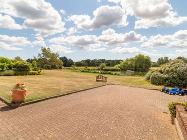 A garden patio with a bench and toy vehicles overlooking a lawn and pond with trees at Horseshoe in Little Glemham near Wickham Market