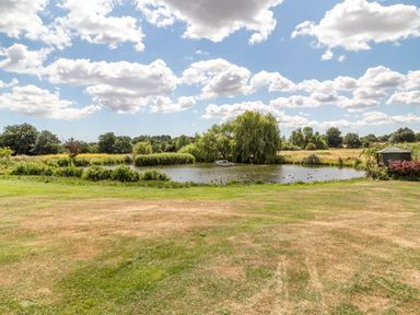 A pond with a boat and trees surrounded by grass and a gazebo in the background at Horseshoe in Little Glemham near Wickham Market