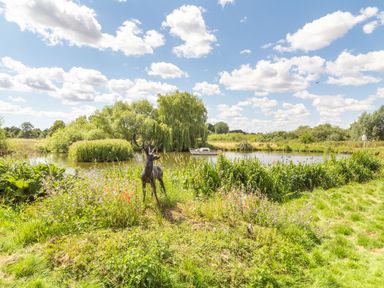 A garden with a metal deer sculpture by a pond with trees and a boat at Horseshoe in Little Glemham near Wickham Market