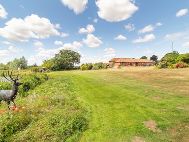 A lawn with flowers and statue of a deer near a red brick house at Horseshoe in Little Glemham near Wickham Market