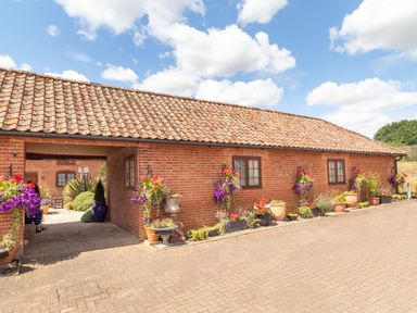 A brick building with tiled roof flowers in pots along the wall and an archway leading to a courtyard at Horseshoe in Little Glemham near Wickham Market