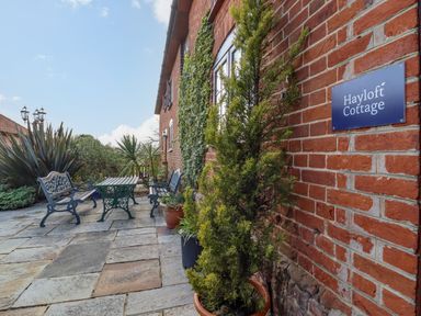 An outdoor patio with stone flooring metal benches and table and plants at Hayloft Cottage Little Glemham near Wickham Market