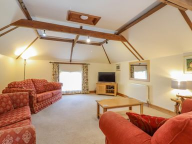 A living room with red patterned sofas a wooden coffee table a television on a wooden stand and exposed wooden ceiling beams at Hayloft Cottage in Little Glemham near Wickham Market