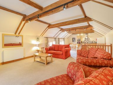 A sitting area with red sofas and a wooden coffee table in a room with exposed wooden beams at Hayloft Cottage in Little Glemham near Wickham Market