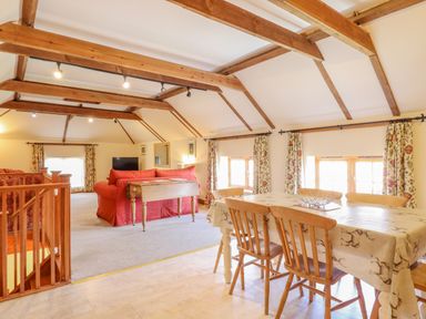 A dining area with a table and chairs next to a living room with red sofas and wooden beams on the ceiling at Hayloft Cottage in Little Glemham near Wickham Market