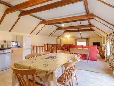 A dining table with chairs in an open-plan kitchen and living area with wooden beams at Hayloft Cottage in Little Glemham near Wickham Market