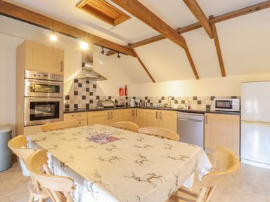 A kitchen with wooden cabinets a dining table and six wooden chairs at Hayloft Cottage in Little Glemham near Wickham Market