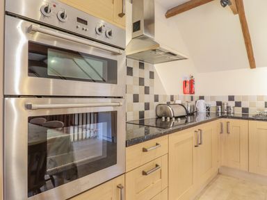 A kitchen with stainless steel double oven wooden cabinets stove and countertop appliances at Hayloft Cottage in Little Glemham near Wickham Market